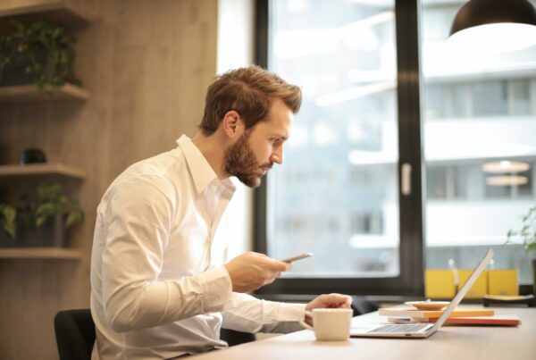 A man sat at his desk on a laptop and mobile.